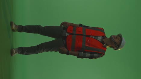 cuerpo lleno de ingeniero masculino asiático con casco de seguridad mirando a su alrededor mientras está de pie en el estudio de fondo de pantalla verde, durante la puesta o el amanecer