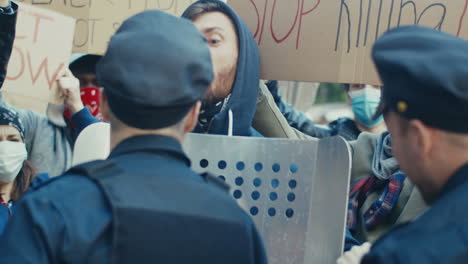 一名白人男子在街上与多民族群体的抗议活动中向一名警察推<unk>和大喊大叫