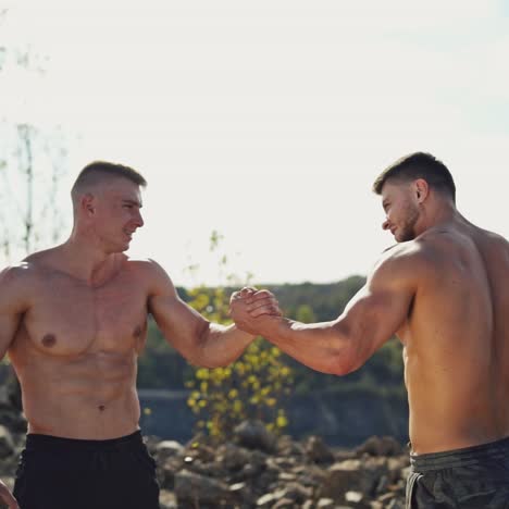 two sportsmen greeting each other on nature background. shirtless bodybuilders with muscular body shaking hands outdoors.