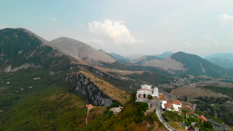 Muñeca-Aérea-En:-Dron-Volando-Hacia-Una-Pequeña-Iglesia-Italiana-Típica-En-Una-Configuración-Extrema-En-La-Cima-De-Una-Colina-Aislada-Rodeada-Por-Una-Vista-Increíble-De-Las-Montañas-En-El-Sur-De-Italia,-Maratea-Basilicata