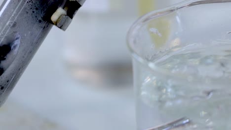 Close-up view of bubbling liquid in a glass beaker with metal tube insertion.