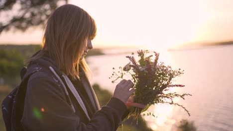 beautiful young woman with a bouquet of wildflowers on the coast at sunset