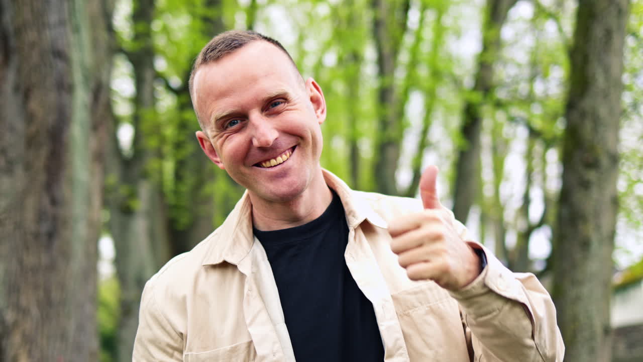 Uomo felice in giacca e occhiali che passeggia all'aperto in un parco verde, usando il telefono cellulare. Concetto di stile di vita urbano in primavera. Uomo che cammina sognante nel parco.