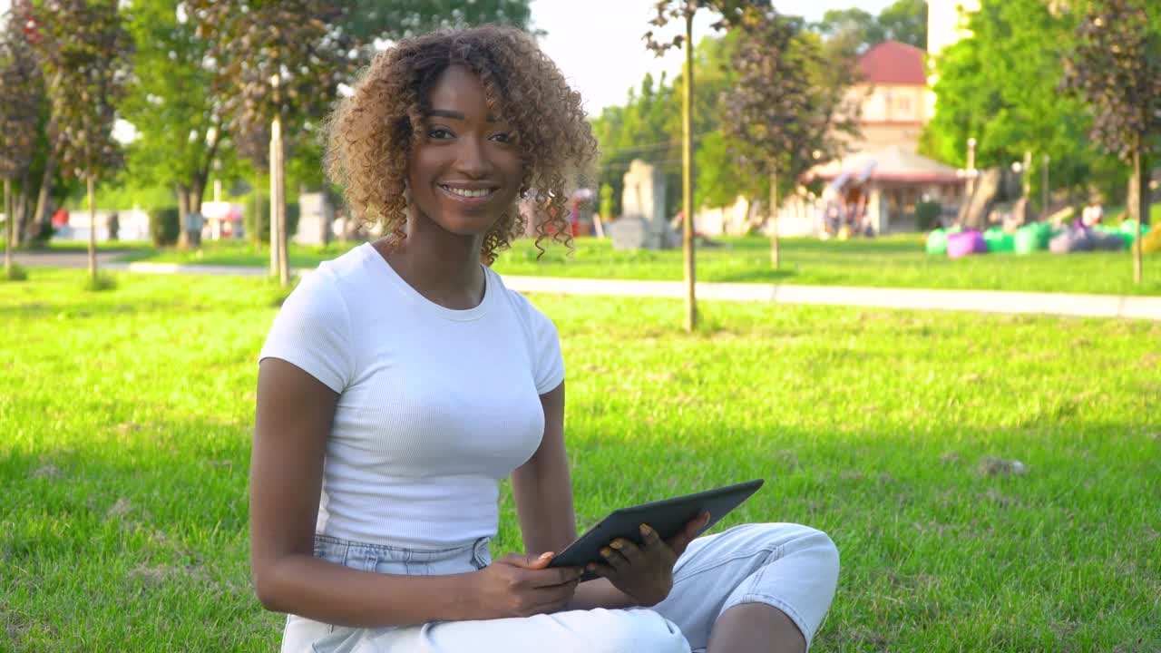 Beautiful smiling confident young african american woman pretty face with tablet looking at camera posing alone at park