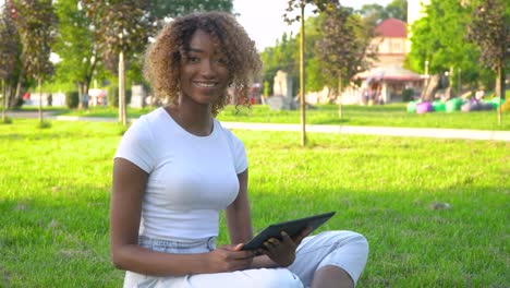 beautiful smiling confident young african american woman pretty face with tablet looking at camera posing alone at park
