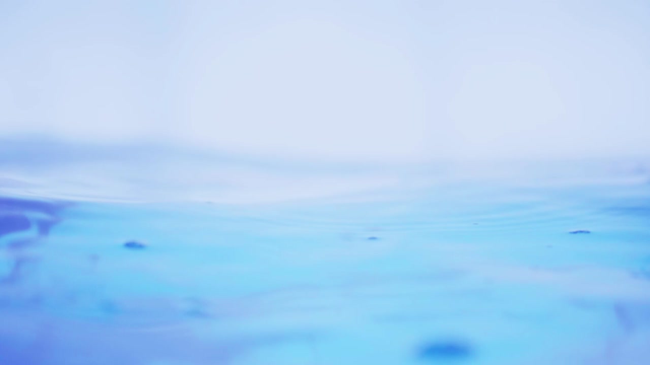 슬로우 모션의 깨끗한 물 표면은 물이 튀는 상점으로 화면을 채우고 기포로 액체 표면을 흔들고 있습니다.