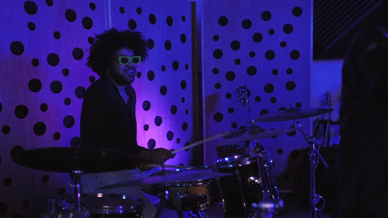 Uomo con capelli afro e occhiali da sole al neon che suona la batteria in uno studio musicale