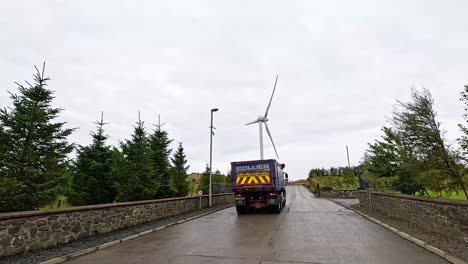 truck travels past windmill on rural road