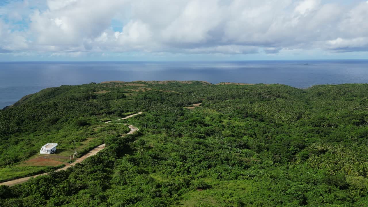 disparo aéreo de avión no tripulado con vistas a la vasta selva de la isla con carretera serpentina frente a la bahía del océano turquesa y el paisaje nuboso en pandan, catanduanes