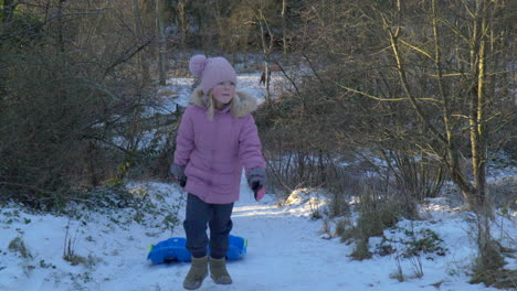 Slowmotion-of-girl-walking-up-a-snow-covered-hill-with-two-bobsleds