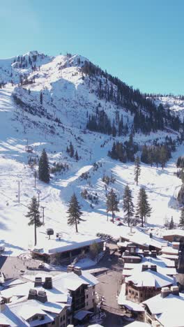 Vertical-Aerial-View-of-Lake-Tahoe-Ski-Resort-on-Sunny-Winter-Day,-Snow-Capped-Palisades,-Olympic-Village