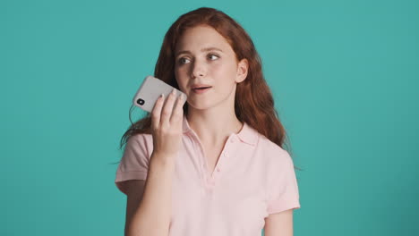 redheaded girl in front of camera on turquoise background.