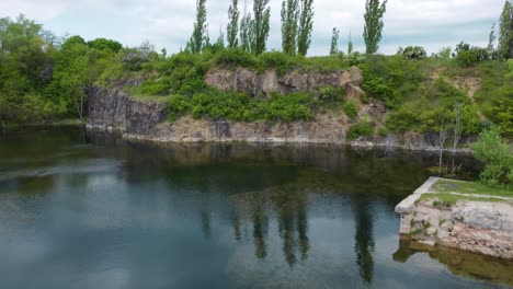 flying over a flooded quarry full of algae towards a cliff with trees above it