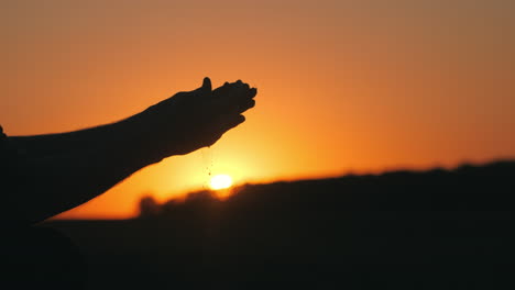 hands releasing sand at sunset