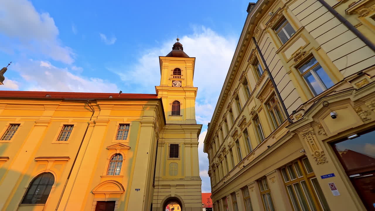 Building with tower clock lit by the golden light of sunset. Low angle view at the facades of the historical buildings of Sibiu, Romania