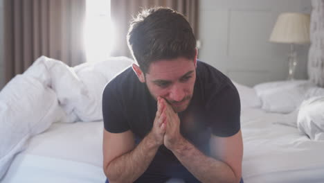 man wearing pajamas suffering with depression sitting on bed at home