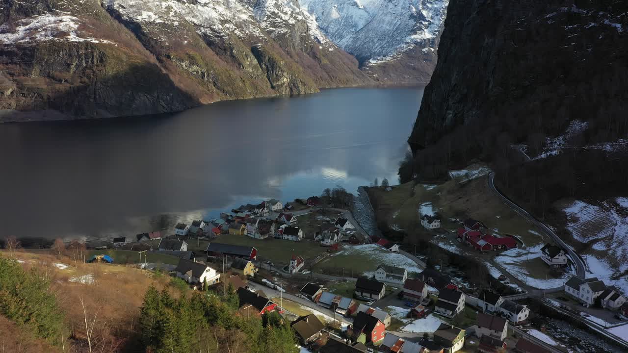 aldea undredal a lo largo de aurlandsfjord en noruega - antena en movimiento hacia adelante desde la ladera con una inclinación lenta hacia arriba desde la aldea para revelar el fiordo y las montañas nevadas en el fondo