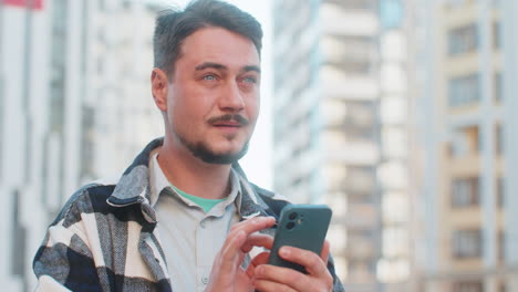 hombre maduro sonriente turista hablando en internet a través de teléfono móvil de pie en la calle del centro de la ciudad