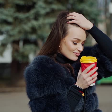 fashion outdoor video of beautiful sensual girl with dark hair wearing luxurious fur coat,holding paper cup with coffee.