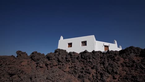 white building standing out against a deep blue sky, built on a solidified lava flow, creating a stark contrast between the smooth white walls and the rough, black volcanic rock