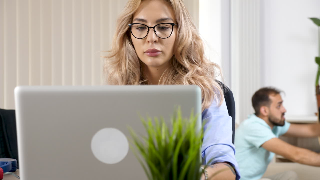 Woman working on laptop at home with man in background