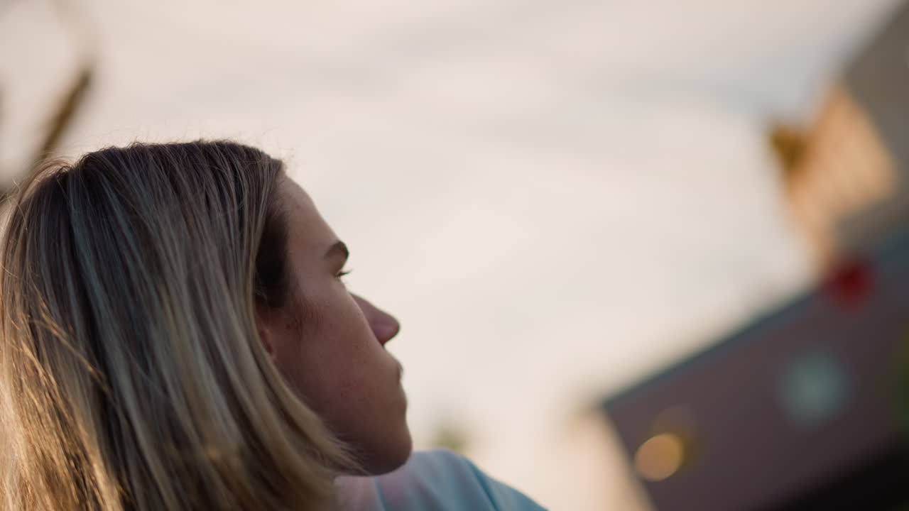 Ragazzina che contempla l'illuminazione festiva. Giovane ragazza che guarda le scene colorate dell'illuminazione della fiera. Giovane donna con meches bionde che contempla l'atmosfera festosa della fiera cittadina durante il tramonto