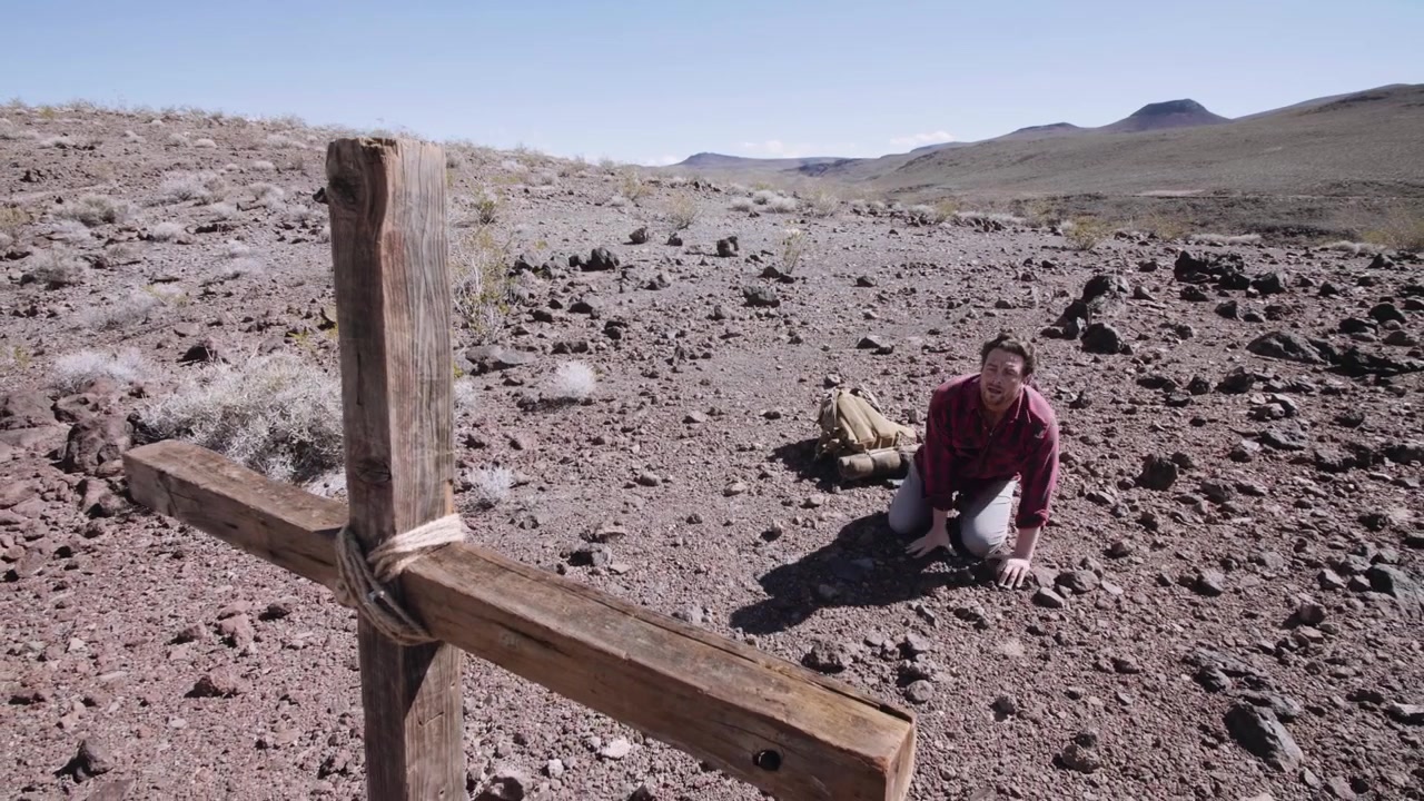 Uomo esausto che si inginocchia e si rialza vicino a una croce di legno nel deserto