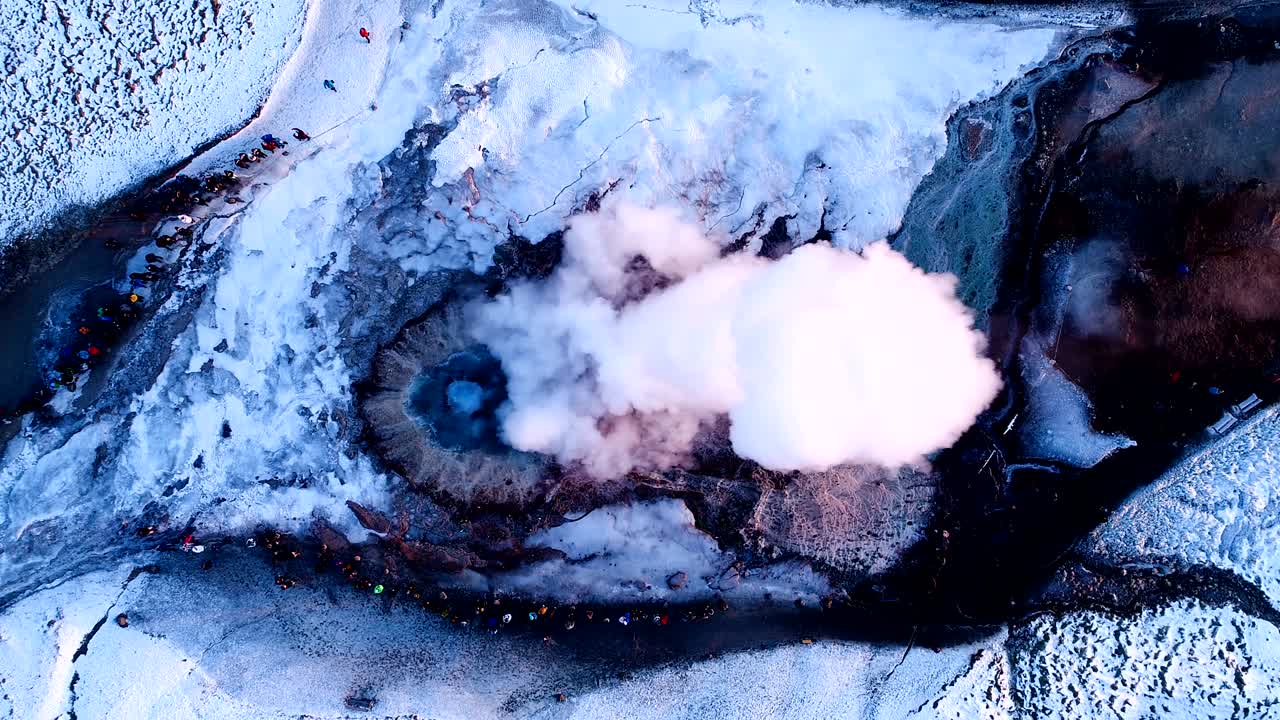 vista aérea sobre un geyser en geysir, islandia. mucho humo está saliendo del geyser con personas caminando alrededor del geyser, bajo la puesta de sol.