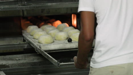 baker pushing the manual loader with dough inside the deck oven and then pulled after placing the bread inside