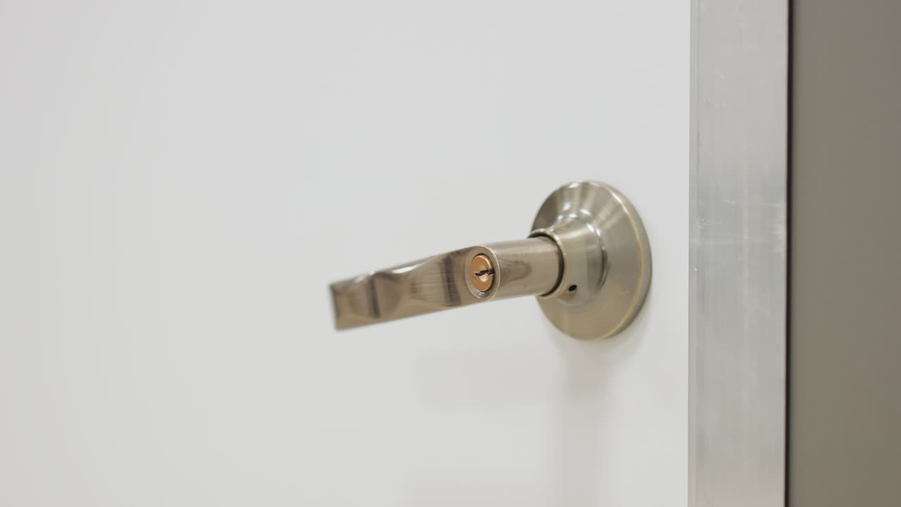 Close up detail of metal door handle as door shuts in bright indoor setting, emphasizing secure closure, minimal modern design, and smooth metallic finish with clean background wall