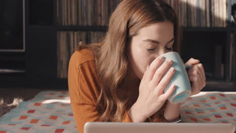 Beautiful-woman-enjoying-using-laptop-online-internet-at-home-drinking-coffee-cosy-apartment