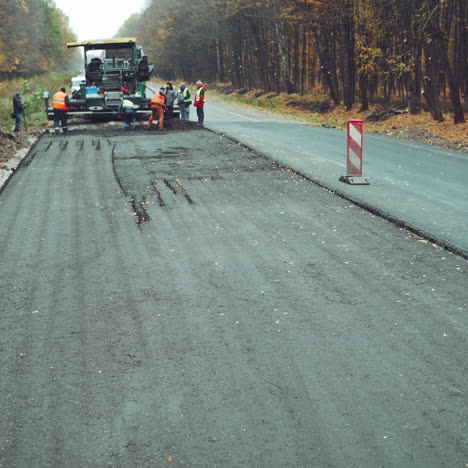 close-up view through the window truck of a new asphalt on the natural background of autumn trees. new bitumen is laying on the road by special machinery equipment and technics.