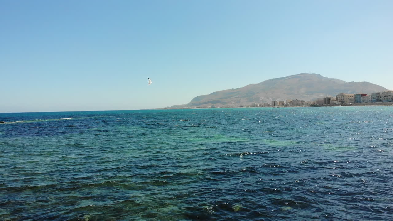 Drone footage flying over clear Mediterranean water toward Monte Erice in Trapani, Sicily