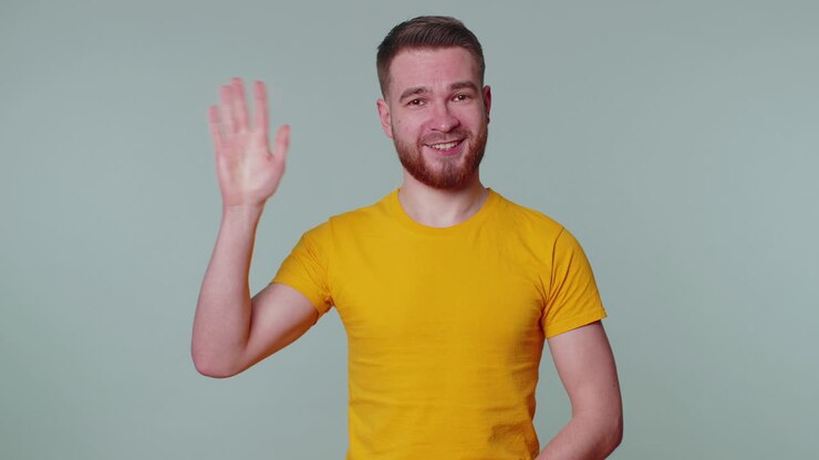 Uomo barbuto che sorride amichevolmente alla telecamera e agita le mani in segno di saluto o addio, accogliente.