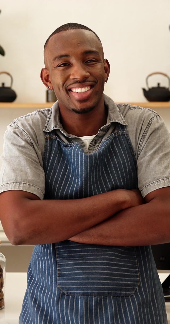 Giovane uomo sorridente con grembiule in piedi in cucina