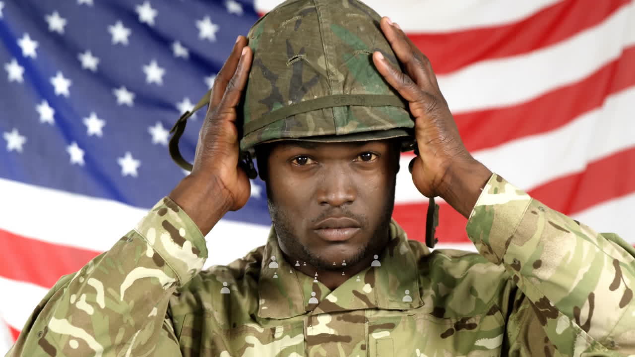 Adjusting helmet, soldier in camouflage stands in front of American flag backdrop