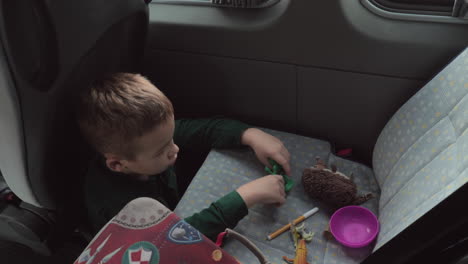 a boy sitting on a cars floor playing with some toys on a back seat