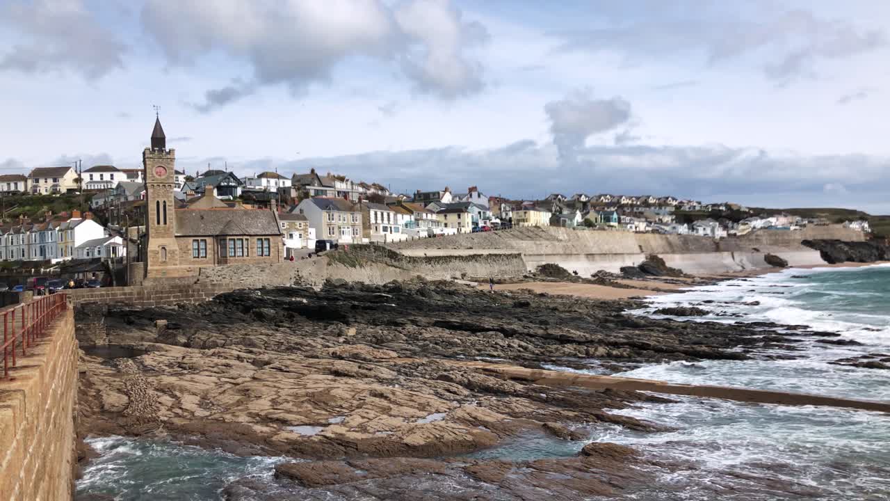 olas del océano en la costa rocosa de porthleven con la ciudad costera y la torre del reloj durante el invierno en helston, inglaterra, reino unido