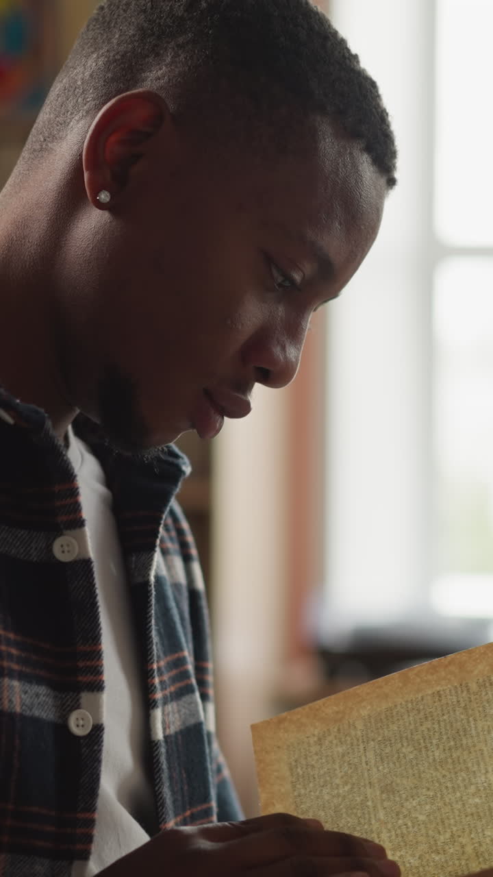 Man reads book in university library. Young African American man interested in scientific article in textbook in information center. Reader holds novel