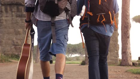 young couple backpackers tourists walking near roman aqueduct arches in parco degli acquedotti park ruins in rome at sunrise with guitar and sleeping bag slow motion steadycam