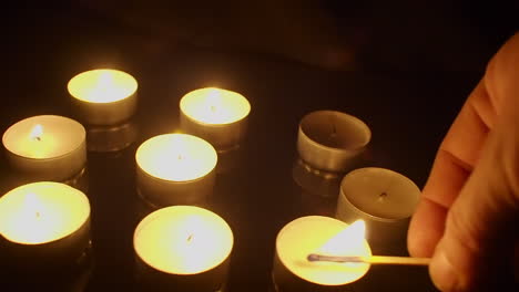 camera dolly shot: tea candles are lit with burning match in dark room