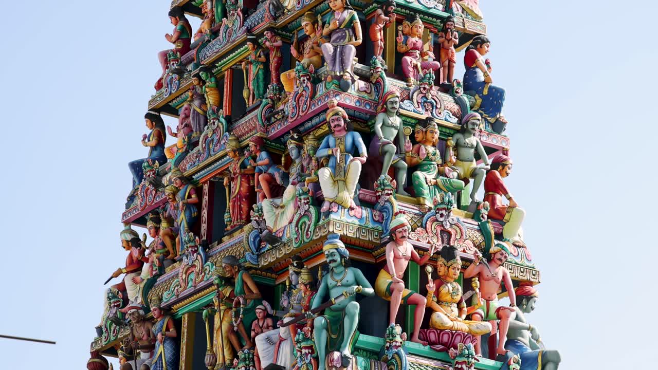 Camera tilts upward along the vibrant, intricately carved gopuram of Sri Mariamman Temple under daylight, highlighting detailed Hindu deities and architectural elements
