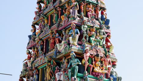 camera tilts upward along the vibrant, intricately carved gopuram of sri mariamman temple under daylight, highlighting detailed hindu deities and architectural elements
