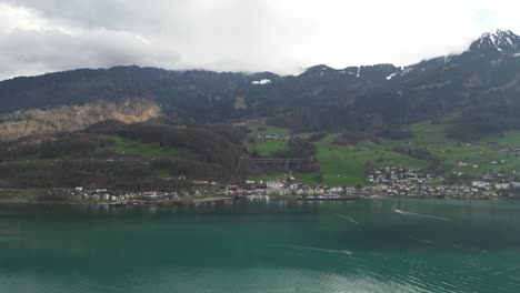 clip de drone sobre el lago ondulado, mostrando el pueblo suizo y las montañas nubladas