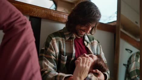 Happy-brunette-guy-in-a-green-checkered-shirt-hugs-his-brunette-girlfriend-in-pink-pants-who-lies-on-his-lap-during-their-vacation-in-a-trailer-outside-the-city-in-a-camp-during-a-picnic-in-the-summer