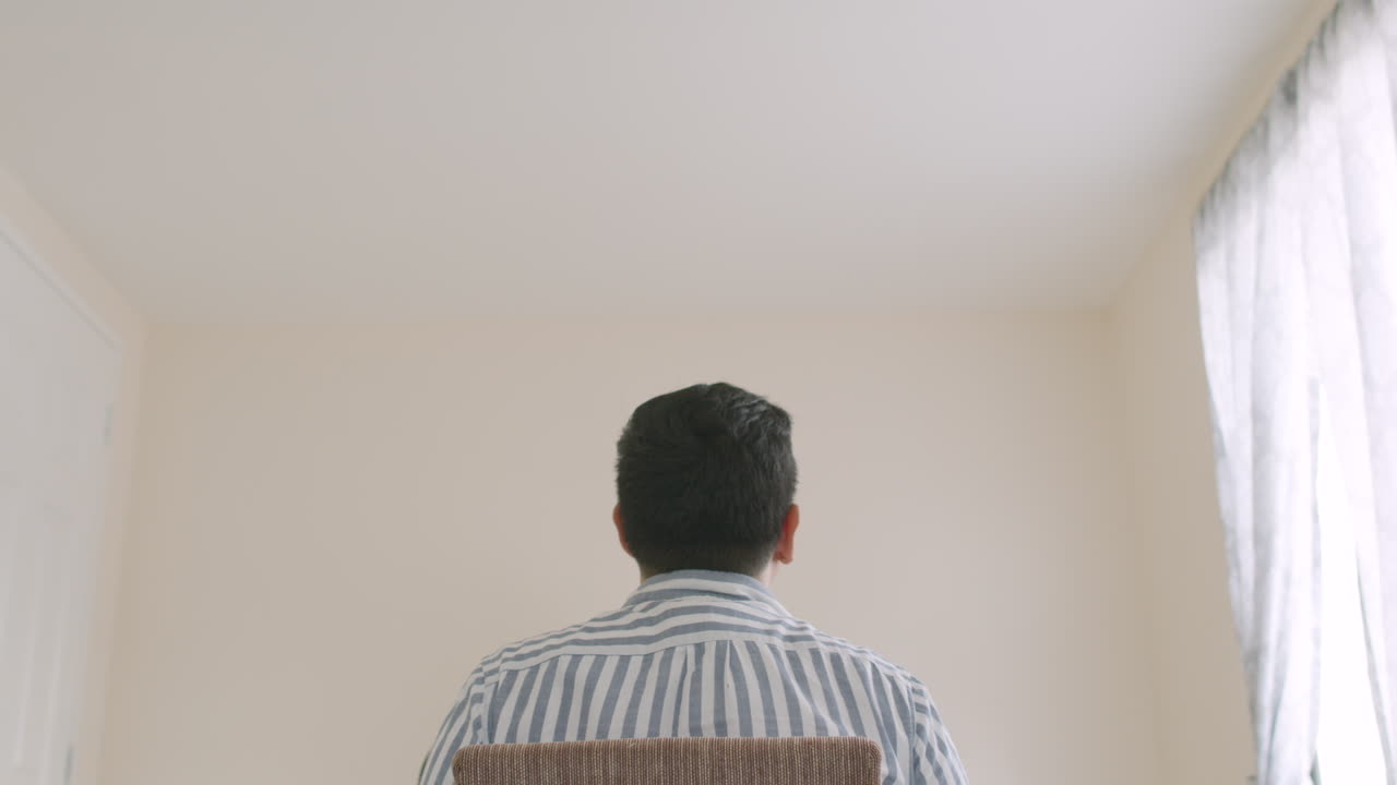 방을 둘러보며 머리를 긁적이며 앉아있는 남자의 뒷모습