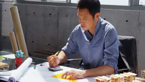 front view of asian male architect working on blueprint at desk in a modern office 4k