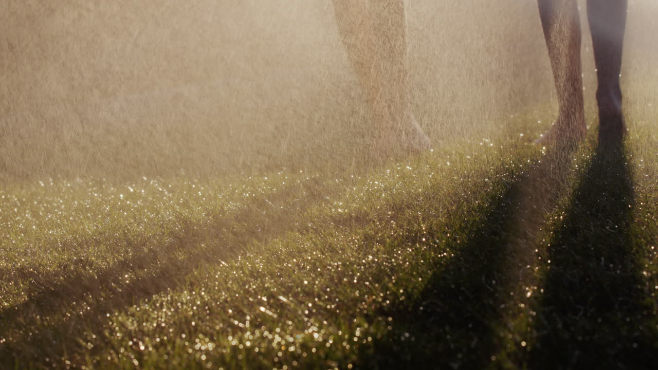 две босые женщины бегают по зеленой траве в струях воды. замедленное движение 4k видео. молодежь и концепция здоровья