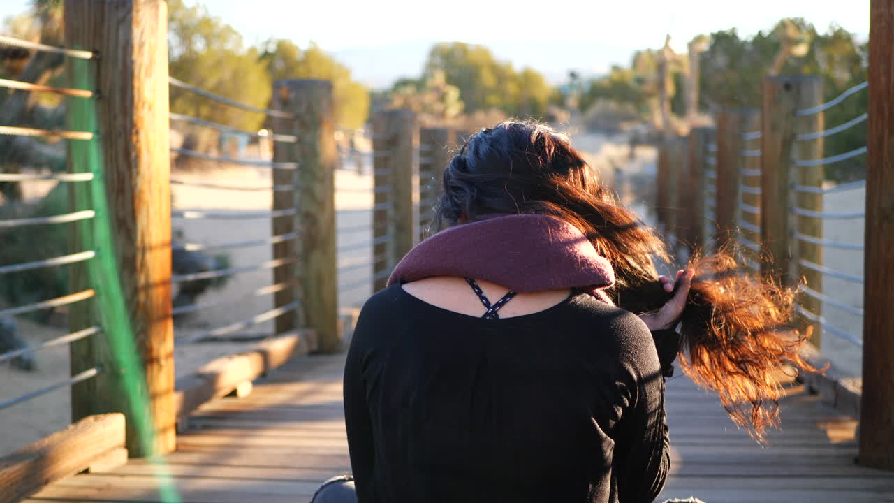 una toma detrás de una hermosa chica en forma con cabello negro sentada y practicando meditación y atención plena en el desierto al atardecer
