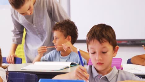 Teacher-assisting-boy-writing-on-notebook-